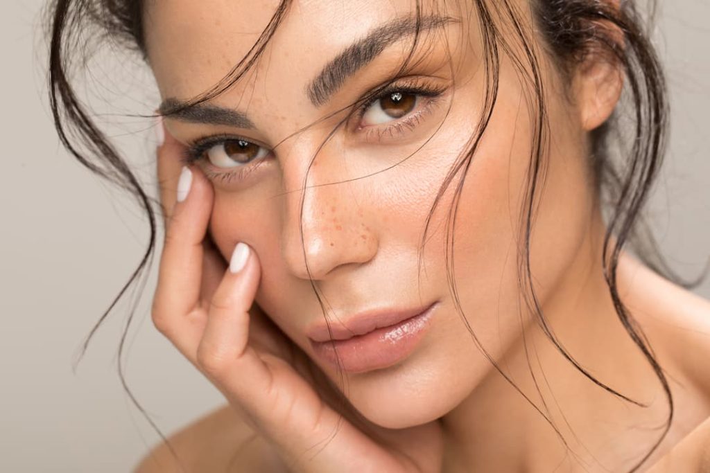 a woman with brown eyes and brown hair touching her face